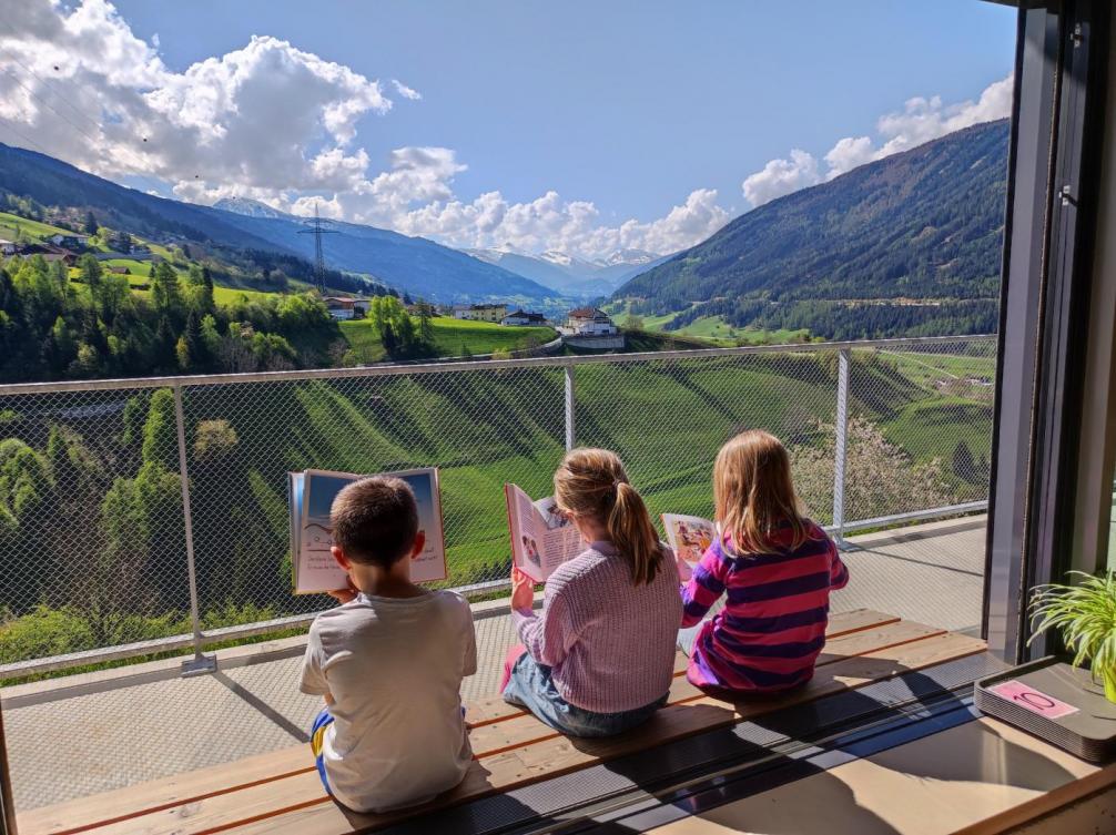 © T.C. | Bildquelle: T.C. | Urheber:in: Thomas Cammerlander Ausblick richtung Matrei, Kinder beim Lesen auf der Terrasse